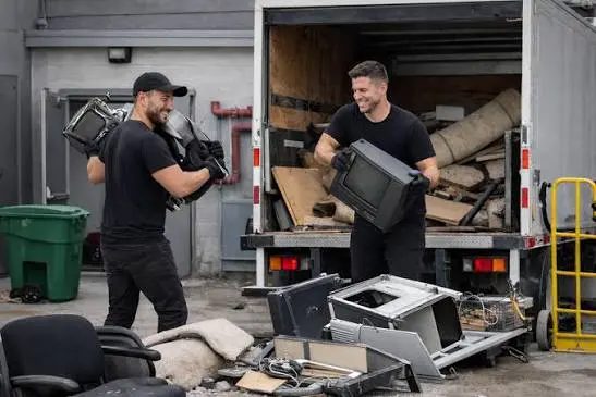 Two crew members carrying old monitors and a television to an open box truck