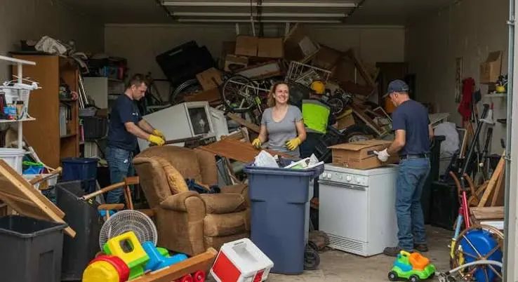 Three people sorting a garage packed with furniture, toys, bins and an old appliance
