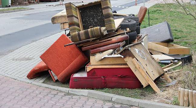 Old armchair, sofa cushions and broken wooden furniture piled at the curb
