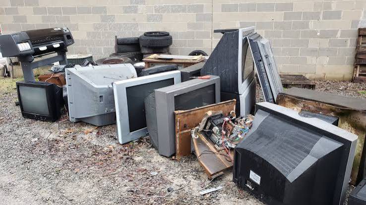 Old tube televisions and a rear-projection TV lined up outside a block wall