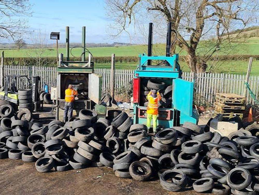 Workers in safety vests baling used tires at an outdoor recycling yard