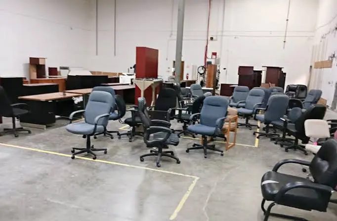 Used office chairs and desks gathered on a concrete commercial floor